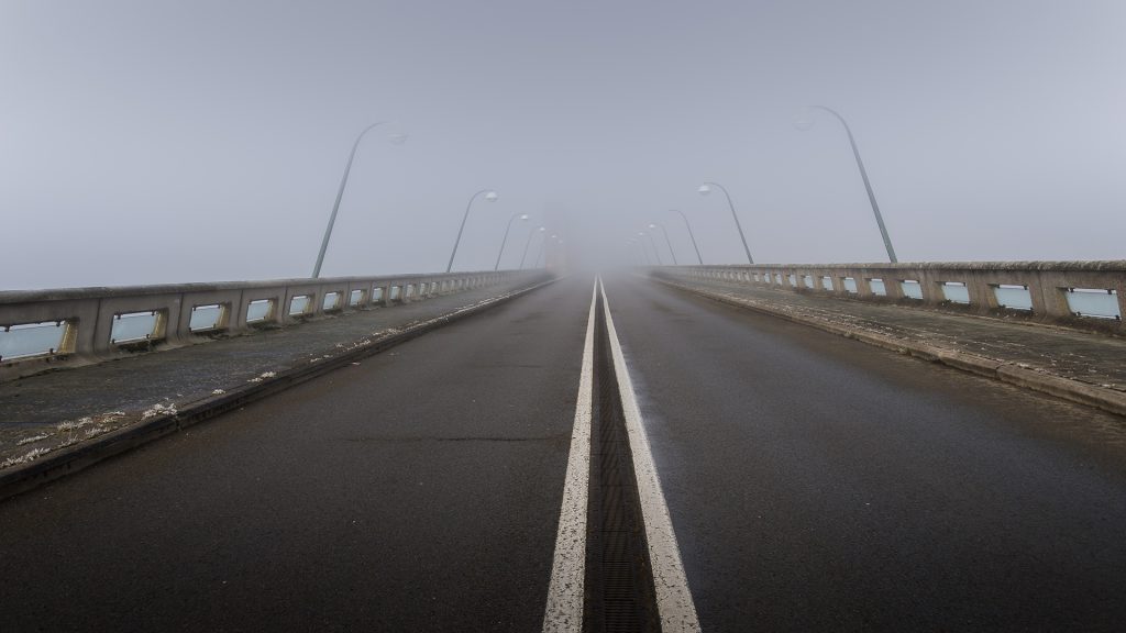 winter landscape photo of a road over a dam in the dense mist