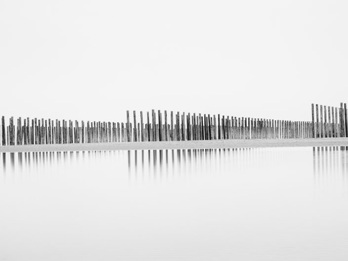 long exposure black and white photo on the beach of the Opal coast in North of France of mussel poles and their reflection