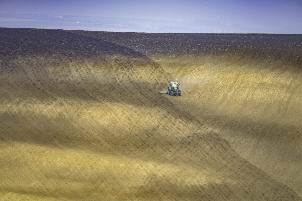 Minimal landscape photo of a rolling hillside field with a tractor as a focal point
