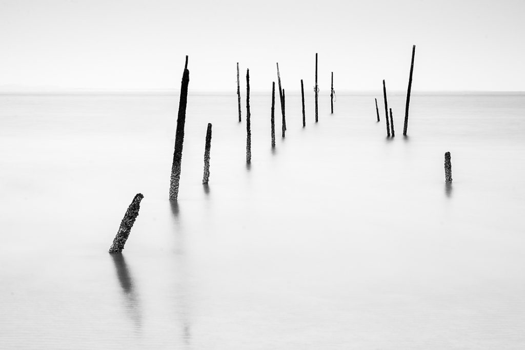 Minimal black and white long exposure landscape photo of poles on the beach of Rockanjke, Netherlands