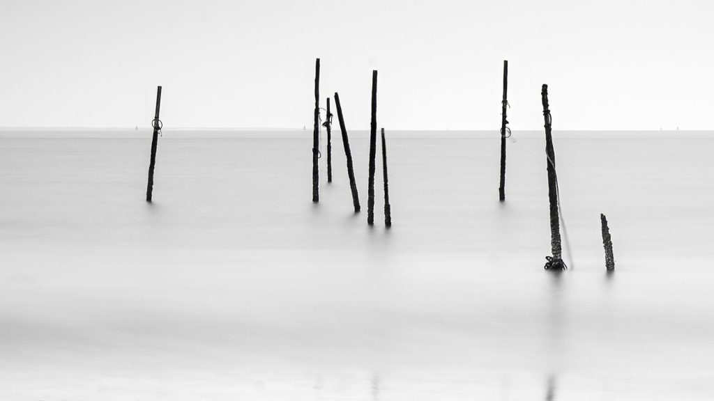 Black-and-white long exposure minimal landscape photo of pole on the Rockanje Beach in the Netherlands
