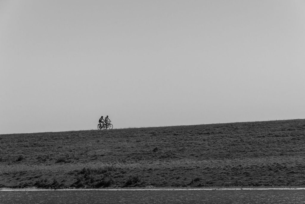 Minimal black-and-white landscape photo of bikers on a dike