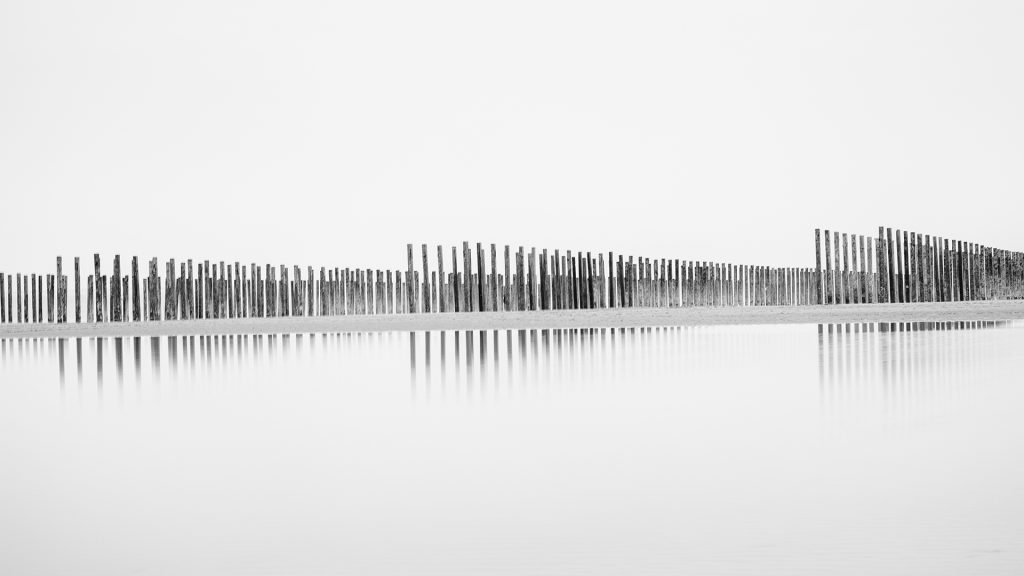 Minimal black and white long exposure landscape of mussel pole reflecting on the beach puddles