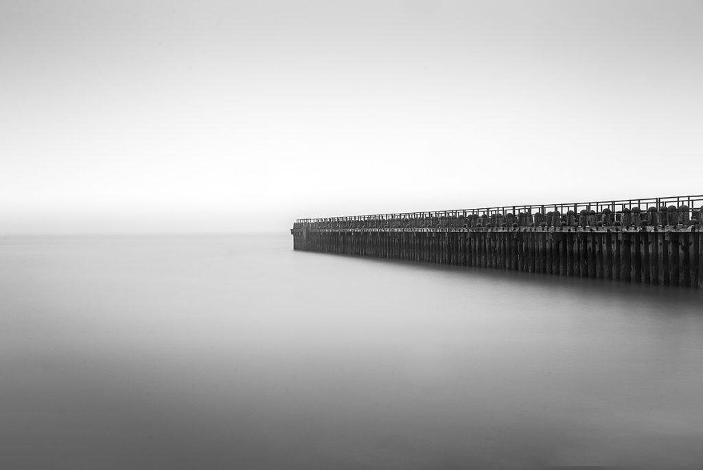 Black-and-white long exposure minimal photo of the jetty in Westkappelle, The Netherlands on a cold misty morning