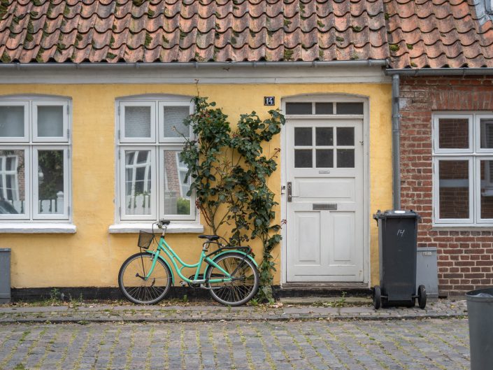 Cityscape photo of a green bike in front of a yellow cottage, Ribe, Denmark