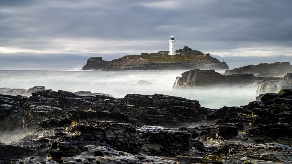 long exposure seascape photo of a lighthouse on an island with wet rock in the foreground