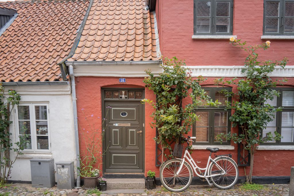Cityscape photo of a tiny red-coloured house and a bike next to the front door.