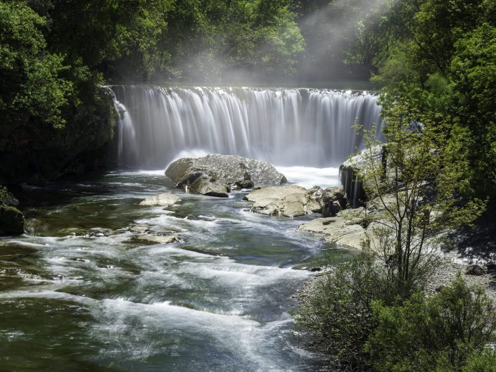 This photo shows a beautiful waterfall surrounded by lush foliage and illuminated by sunbeams. The waterfall cascades into a serene river (Vis), creating a mist that softens the scene. The rocks add an earthy element to this captivating and inspiring view. For this photo, I used a tripod, a polariser, and an ND filter to achieve a longer shutter speed and smoother water on a bright day. 