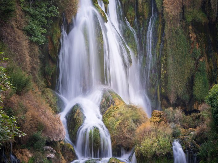 This photo shows a majestic waterfall hidden in a lush, green landscape in Bosnia i Herzegovina. The image evokes a sense of peaceful isolation and highlights the pristine beauty of nature while it can be teeming with tourists there. The photo a great example of the use of long shutter speed, resulting in the soft, almost silky effect of the falling water. The use of vertical and diagonal lines creates a dynamic but balanced image. The lighting is soft and diffuse, creating a dreamy effect and showing off the texture of the water and plants well. The colours are harmonious and varied, adding depth to the picture.