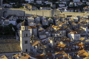 The image shows a classic Dubrovnik (Croatia), with a maze of terracotta roofs under a warm evening light. In the foreground is a striking church tower with a dark dome, and an imposing city wall runs in the background.
Artistic:
The atmosphere is nostalgic and warm, bathed in golden evening light. The stacking of roofs, the stone tones, and the play of light and shadow create a picturesque scene resembling a still life with urban layers. The presence of modern elements does not make it timeless.
